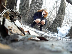 Ginger bridesmaid makes water behind a tree in the forest