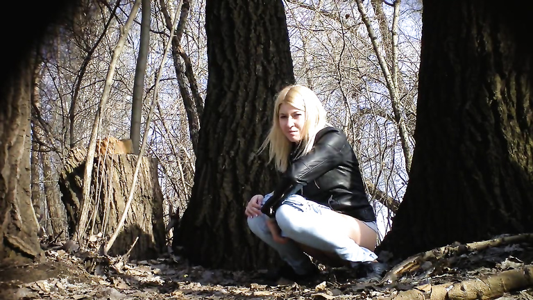 Irresistible girl holds onto jeans while piddling in the city park