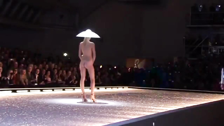 Seductive fashion model in a weird hat walks down the catwalk in the nude