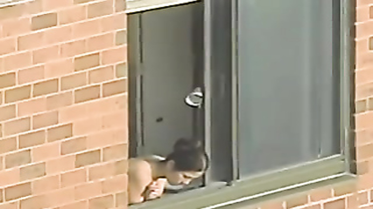 Topless woman looks out her window